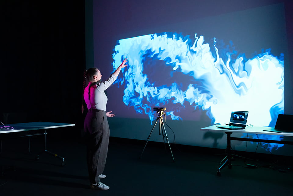 student interacting with art that is projected on a wall - art is a purple visualisation of waves.