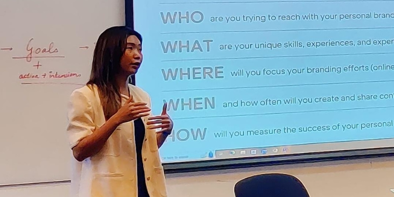 Photo of a guest lecturer presenting in front of the interactive whiteboard titling 5w1h framework to the students who are sitting with their electronic devices