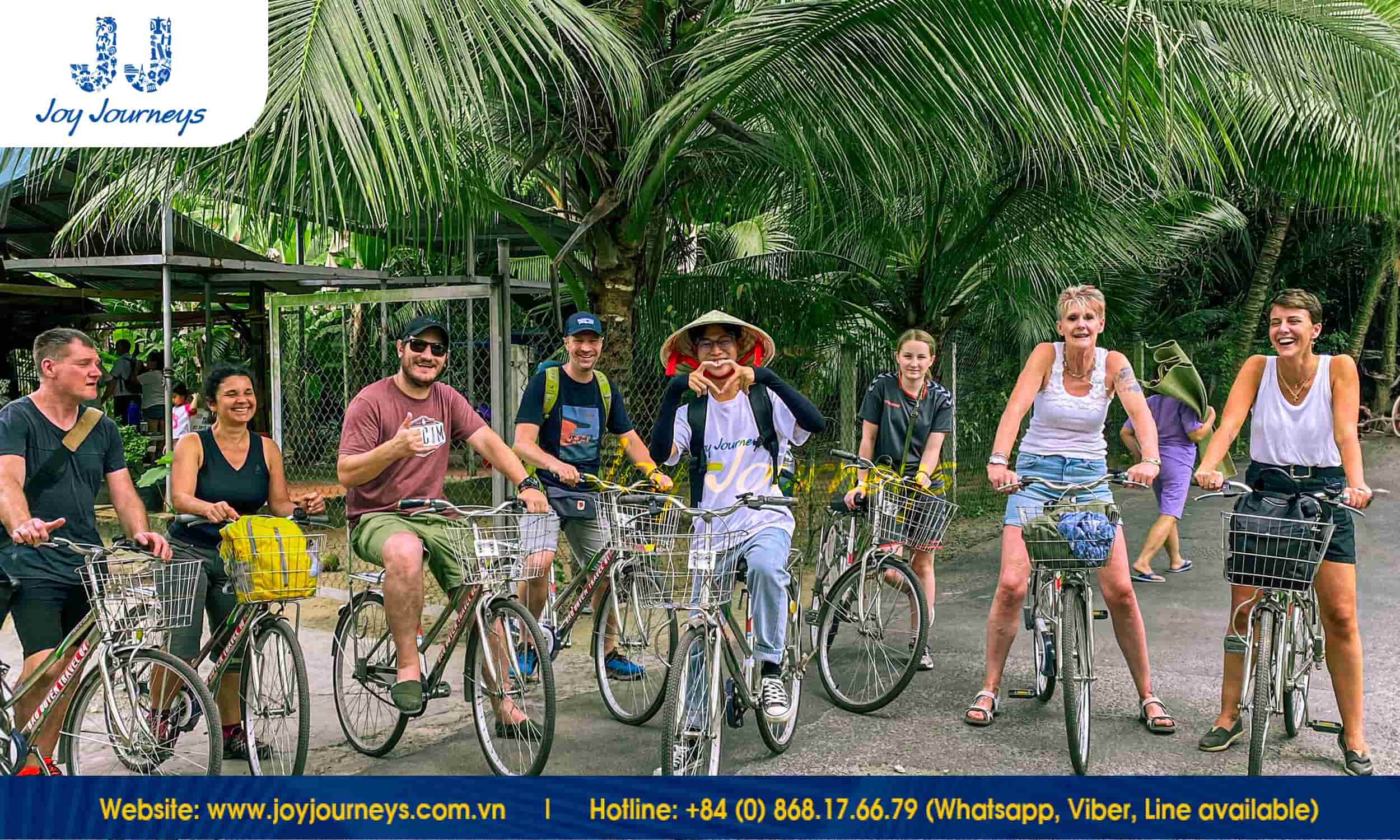 Group of tourists on bicycles pose for a photo under lush palm trees during the Mekong Delta Day Tour – Ben Tre Discovery organised by Joy Journeys.