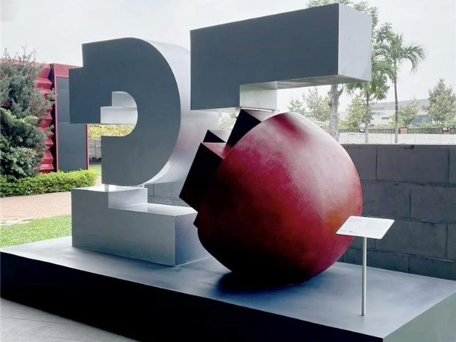 Photo of a modern sculpture of the number 25 with a cracked red sphere in an outdoor setting