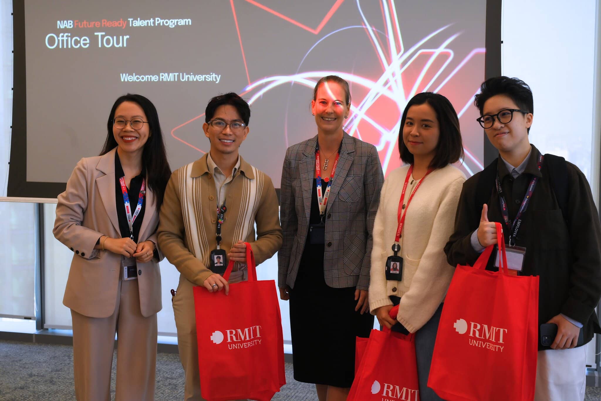 Four people posing with RMIT gift bags during an indoor event