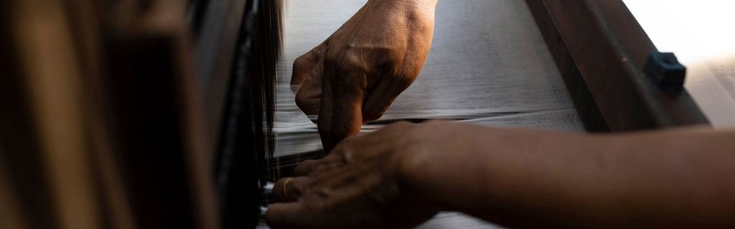 Hands weaving fabric on a traditional wooden loom.