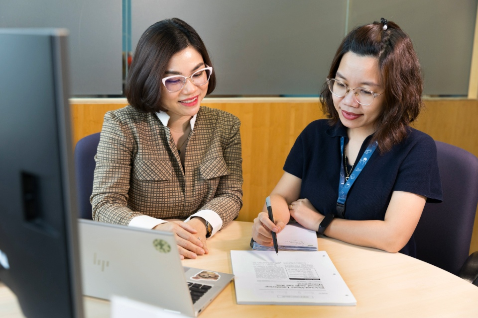 5 women of Asian appearance in front of 2 laptops behind a desk, next to white RMIT craft bags. 