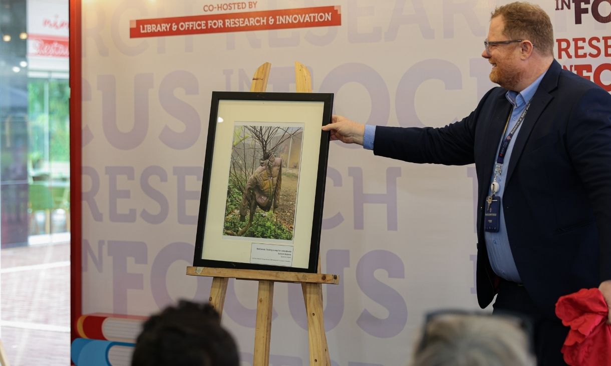 The photo of a man, dressing formally, holding a photo frame with one hand. 