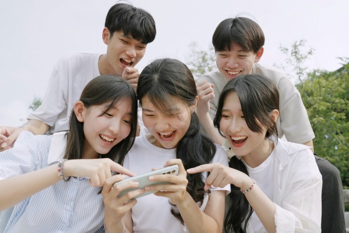 Asian teengers laugh while looking at a smartphone