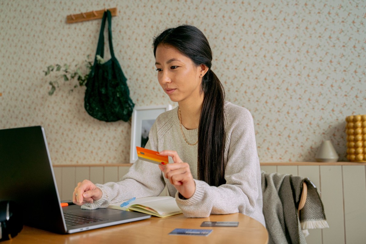 Một phụ nữ cầm thẻ ngân hàng thanh toán trên máy tính