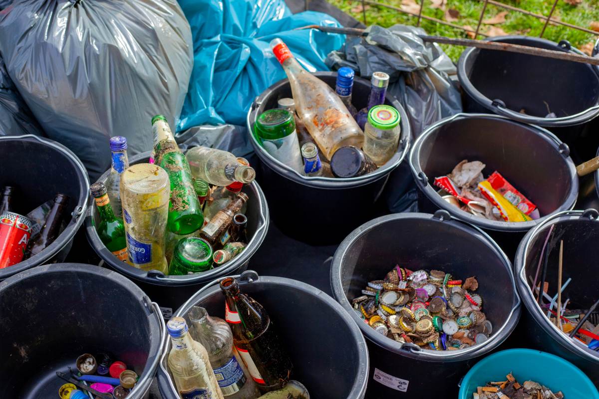 Sorted waste in buckets, including glass bottles, cans, plastic items, and mixed recyclables.