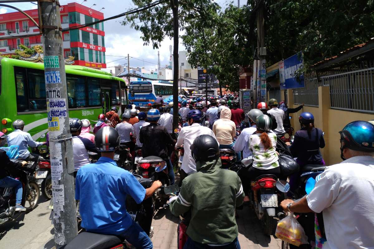 Heavy traffic congestion with dozens of motorcyclists and two buses crowded on a narrow urban street in Vietnam during daytime.