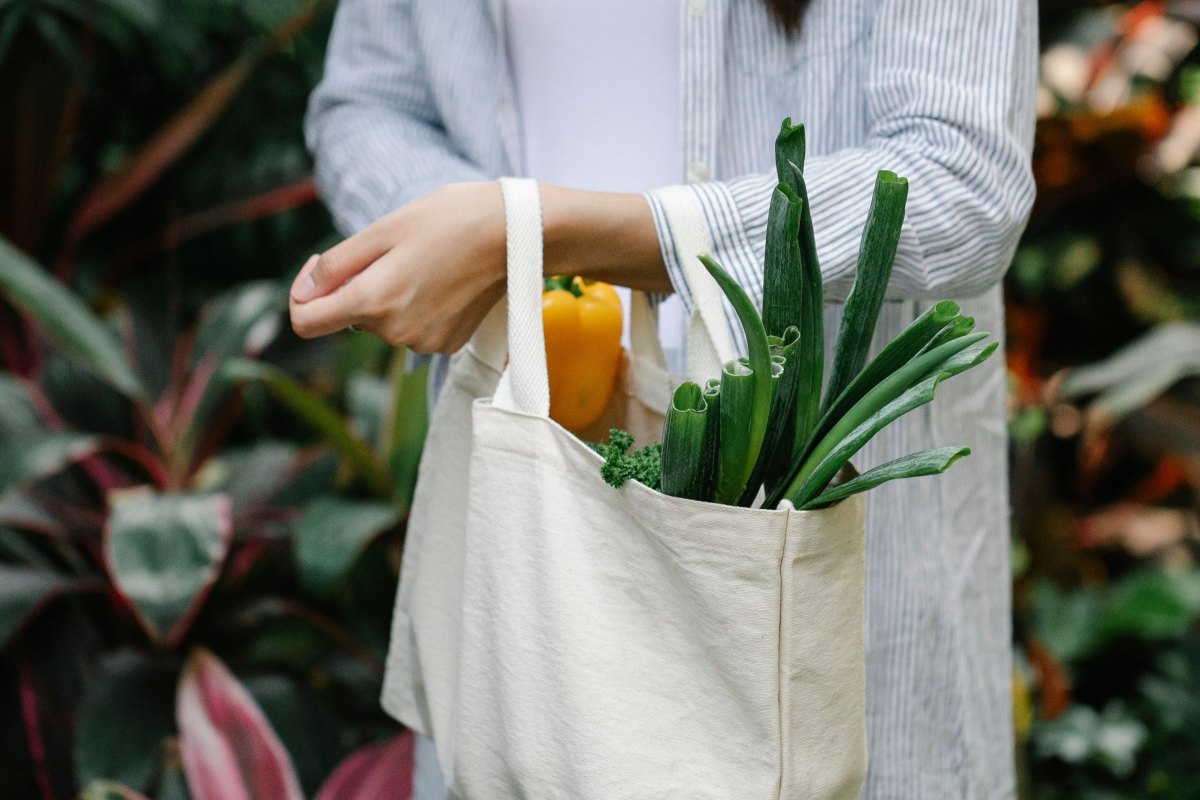Reusable canvas tote bag filled with fresh vegetables, including spring onions and a yellow bell pepper.