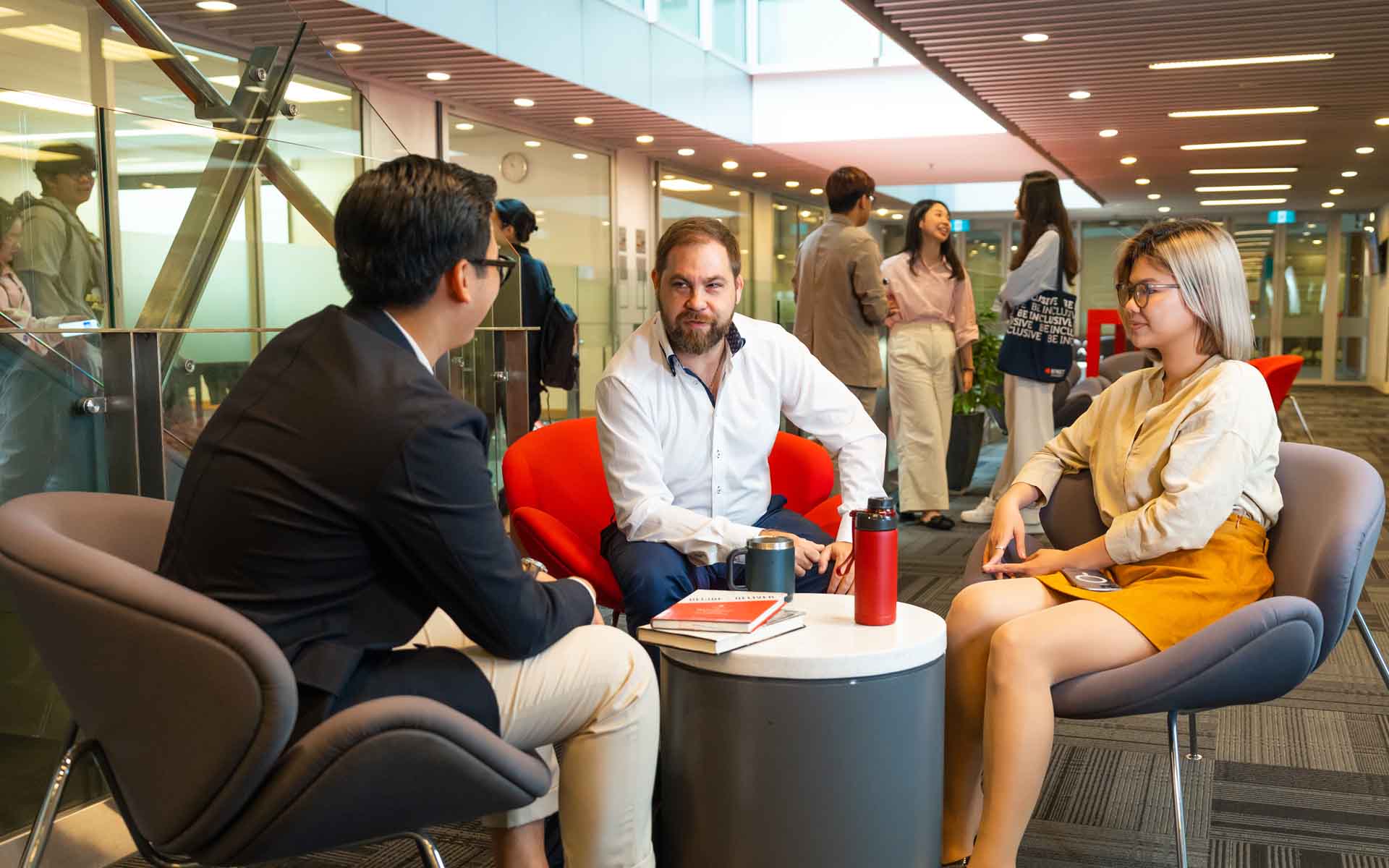 three post graduate business students sitting at campus and have a conversation