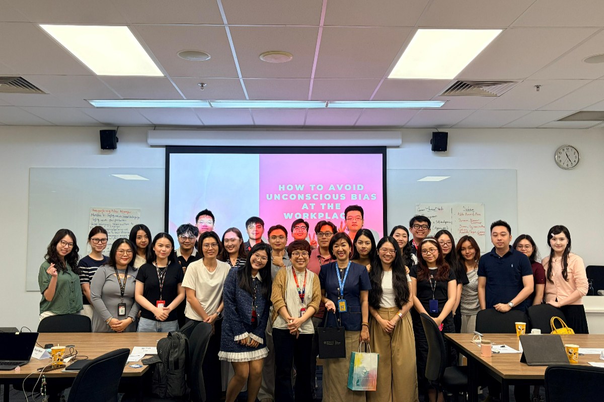 Group photo of a People and Organisations class standing together in a classroom, with a presentation slide behind them titled “How to avoid unconscious bias at the workplace.”