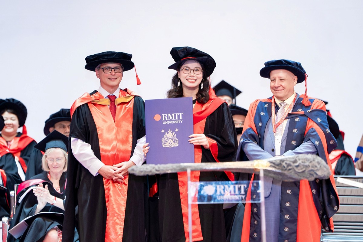 Dr Pham Thanh Hang at the centre holding an RMIT University certificate and smiling during a graduation ceremony.