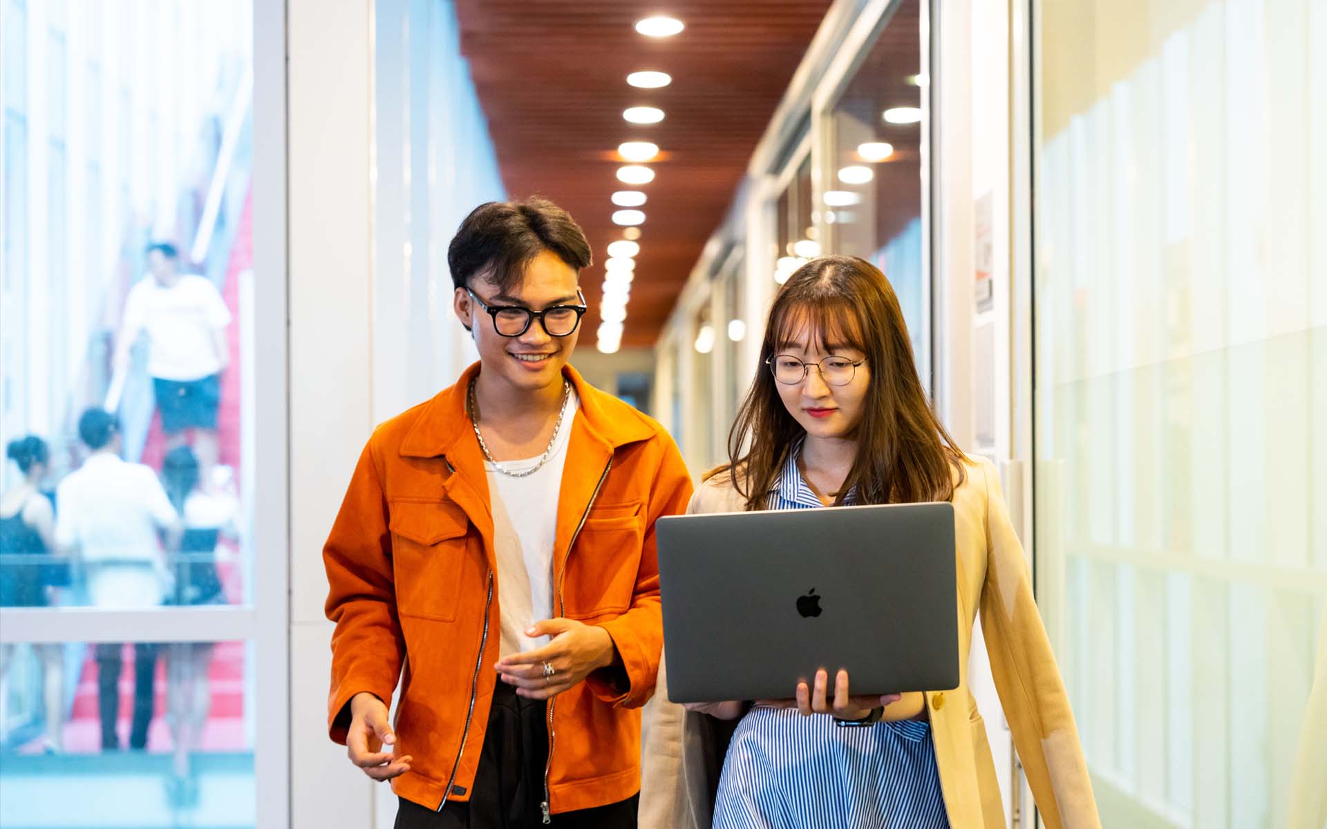 two students one male and one female walking in the office hallway