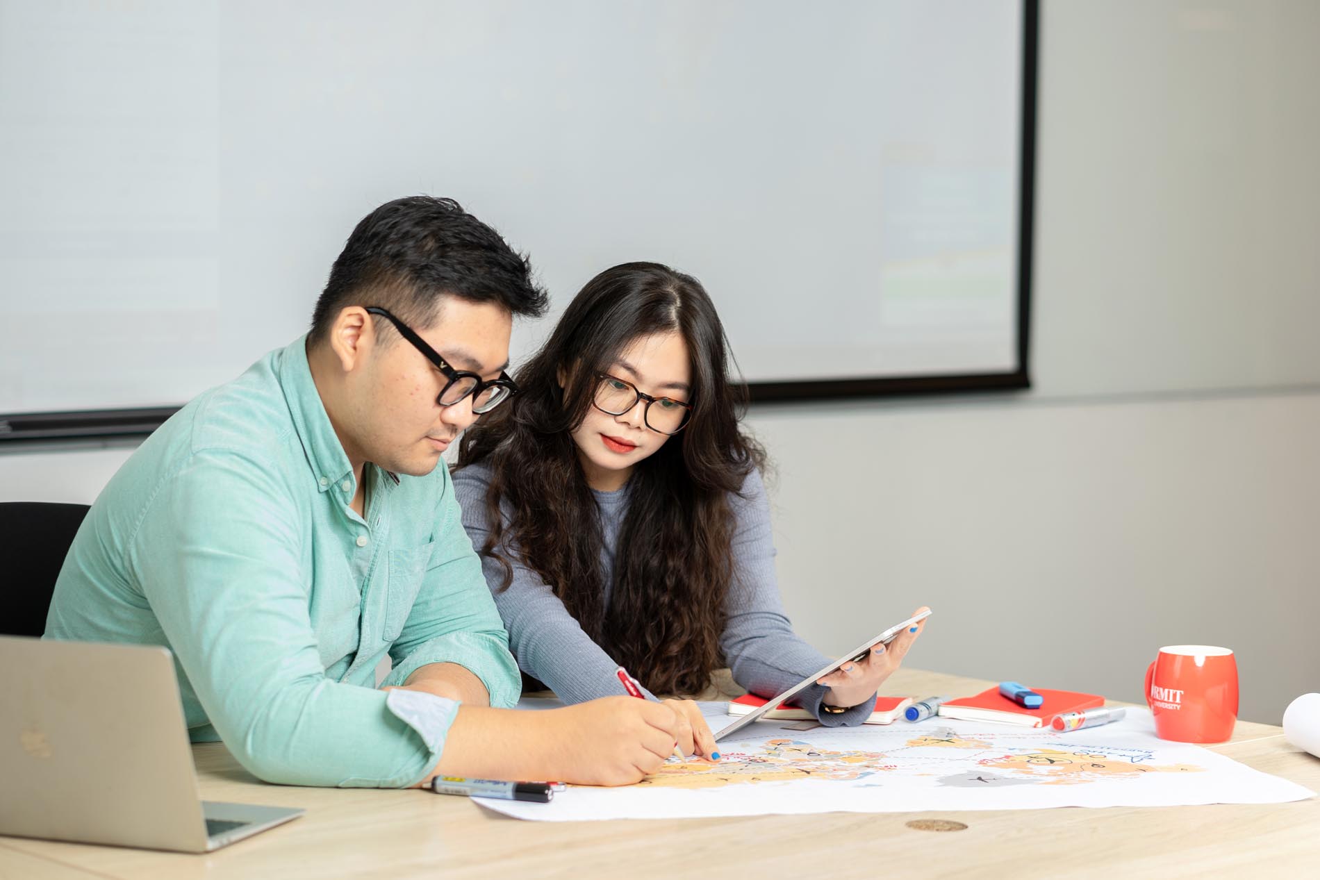 Two students are discussing work on a tablet and map