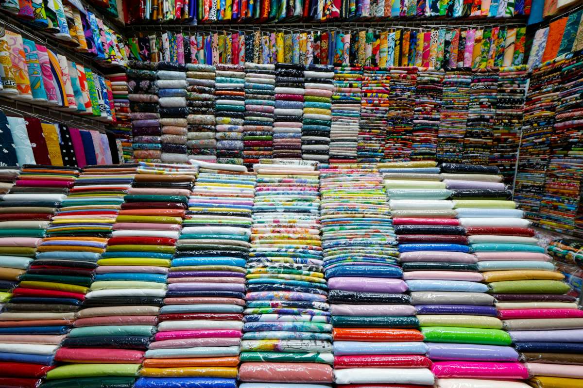 A variety of colourful woven textiles, patterned fabric bags, and handmade dolls displayed together, showcasing vibrant traditional designs.