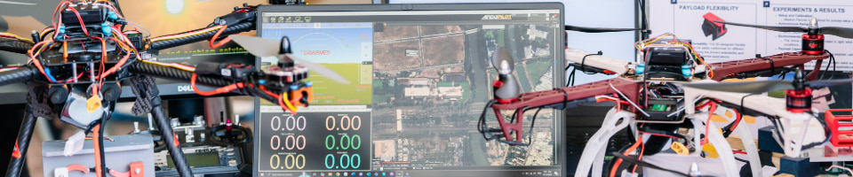 A photo showing two drones sit in front of a computer monitor displaying drone control software with a satellite map at a student project showcase event at RMIT Vietnam.