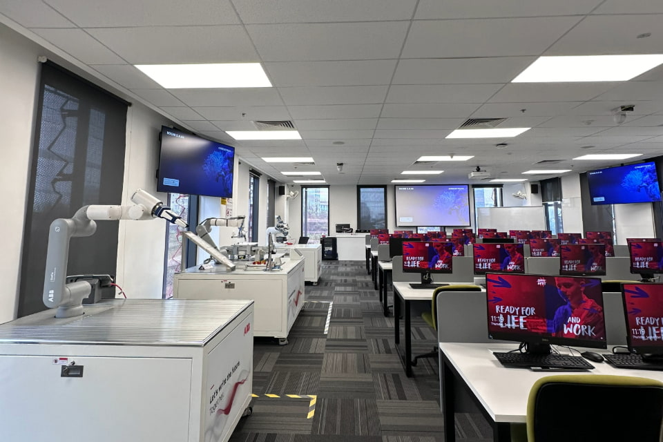 Photo of a computer lab featuring both Linux and Windows with a big whiteboard screen in the front and several TV screen mounted on the wall throughout the lab