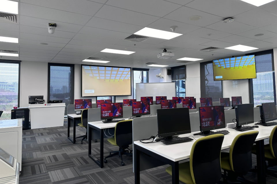 Photo of a lab featuring computer stations and a big whiteboard interactive screen and a tivi screen mounted on the wall