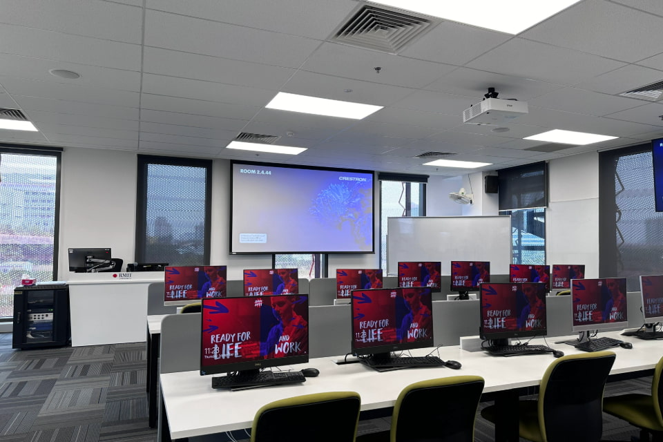 Photo of a computer lab featuring Windows OS system computer stations, with a big interactive board in front of the class and a projector mounted on the ceiling