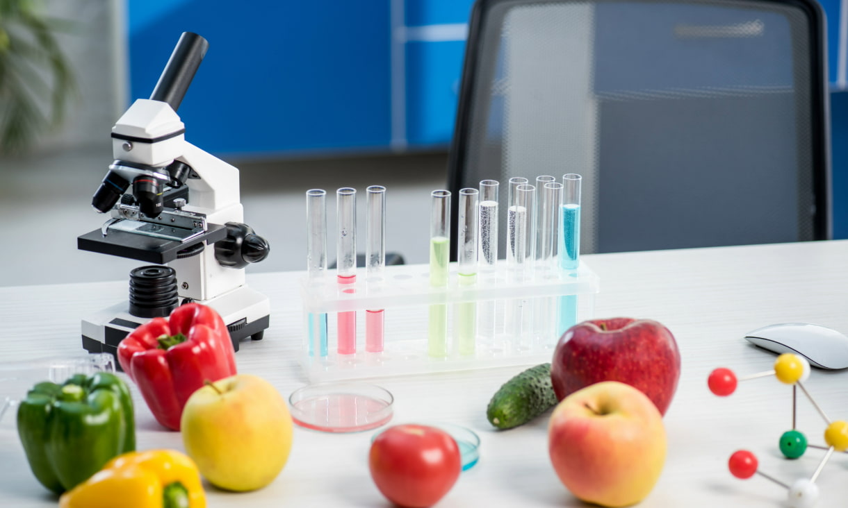 Stock photo of a laboratory setup with test tubes, microscope, and various fruits and vegetables, illustrating the intersection of food technology and nutrition science.