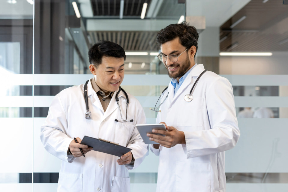Photo of two male Asian doctors holding notebooks and discussing with each other