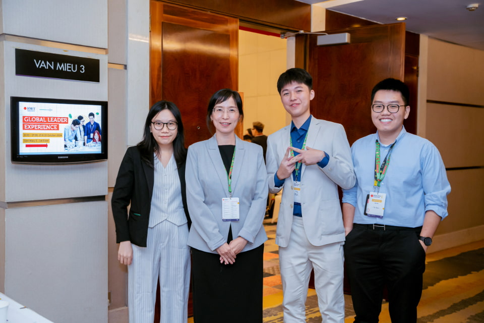 Photo of a professor with her three students smiling at the camera at a conference hall
