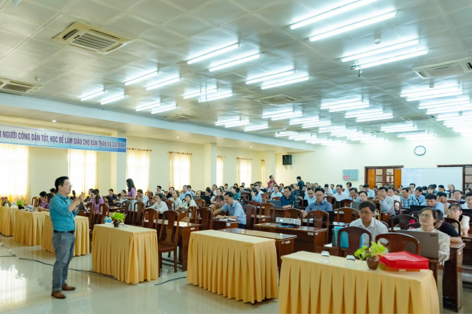 Photo of a speaker presents to a large audience in a well-lit conference room in Vietnam filled with attentive participants seated at tables.
