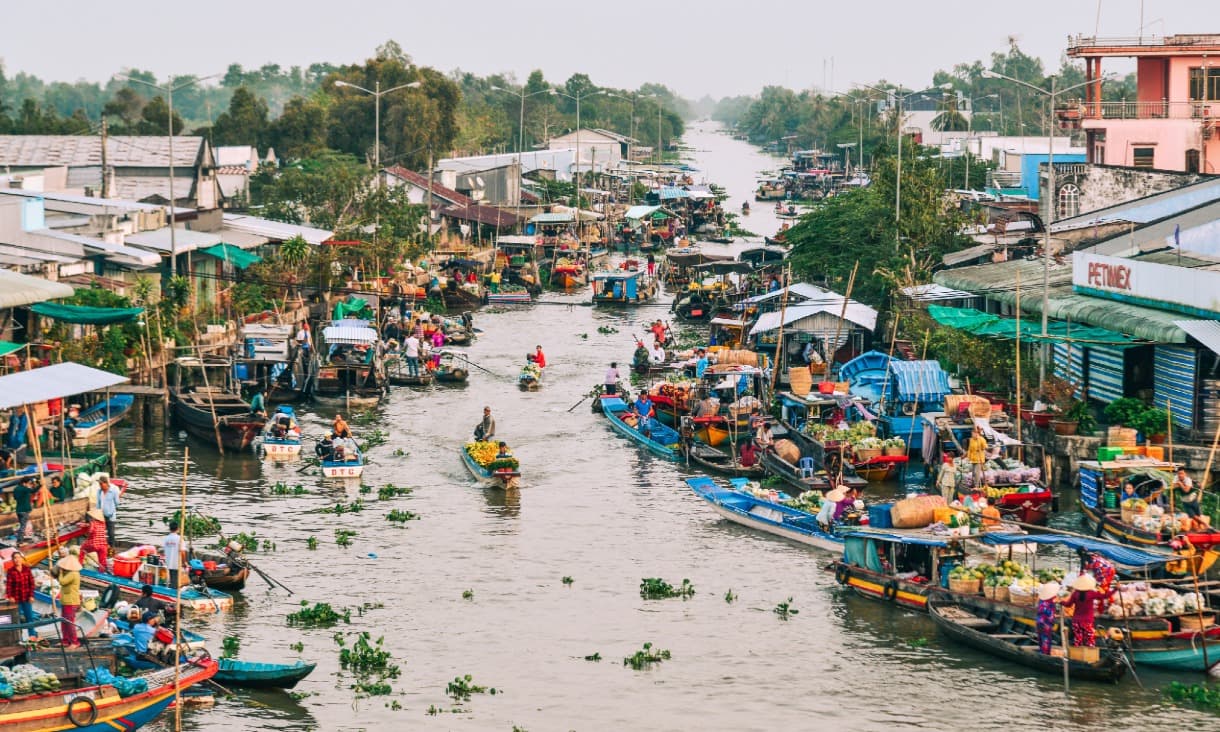 Busy floating market with boats and vendors on a river crowded with goods and people.
