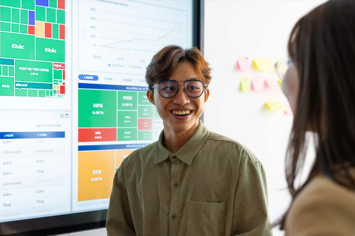 Photo of two students smiling and discussing in front of an interactive white board displaying charts