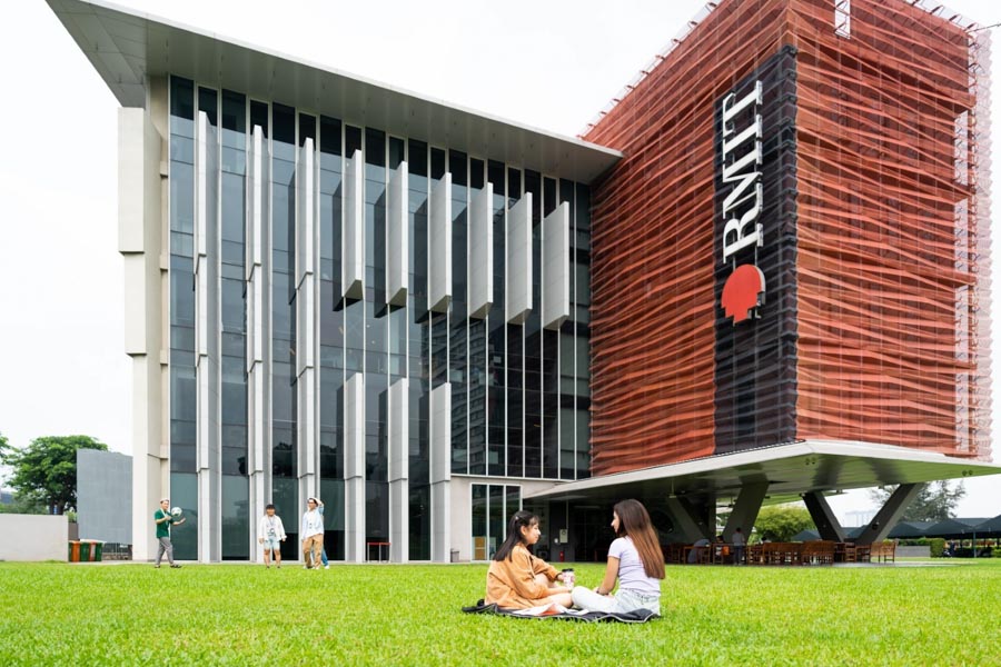 Photo of RMIT Saigon South Campus with two students relaxing on the grass field and three other students playing with a ball at the back