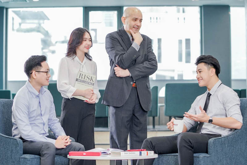Photo of a group discussion of four professionals in business attires, with one person holding a book titled 'Risk Intelligence'