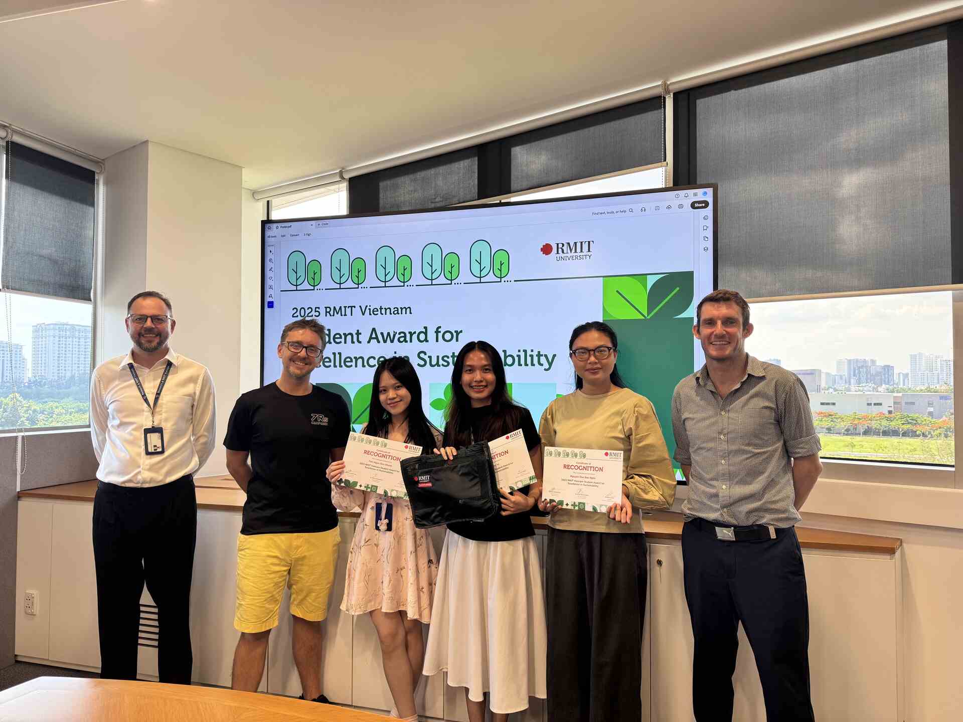 Six people stand in a classroom, with three students holding certificates in front of a screen displaying “2025 RMIT Vietnam Student Award for Excellence in Sustainability.”