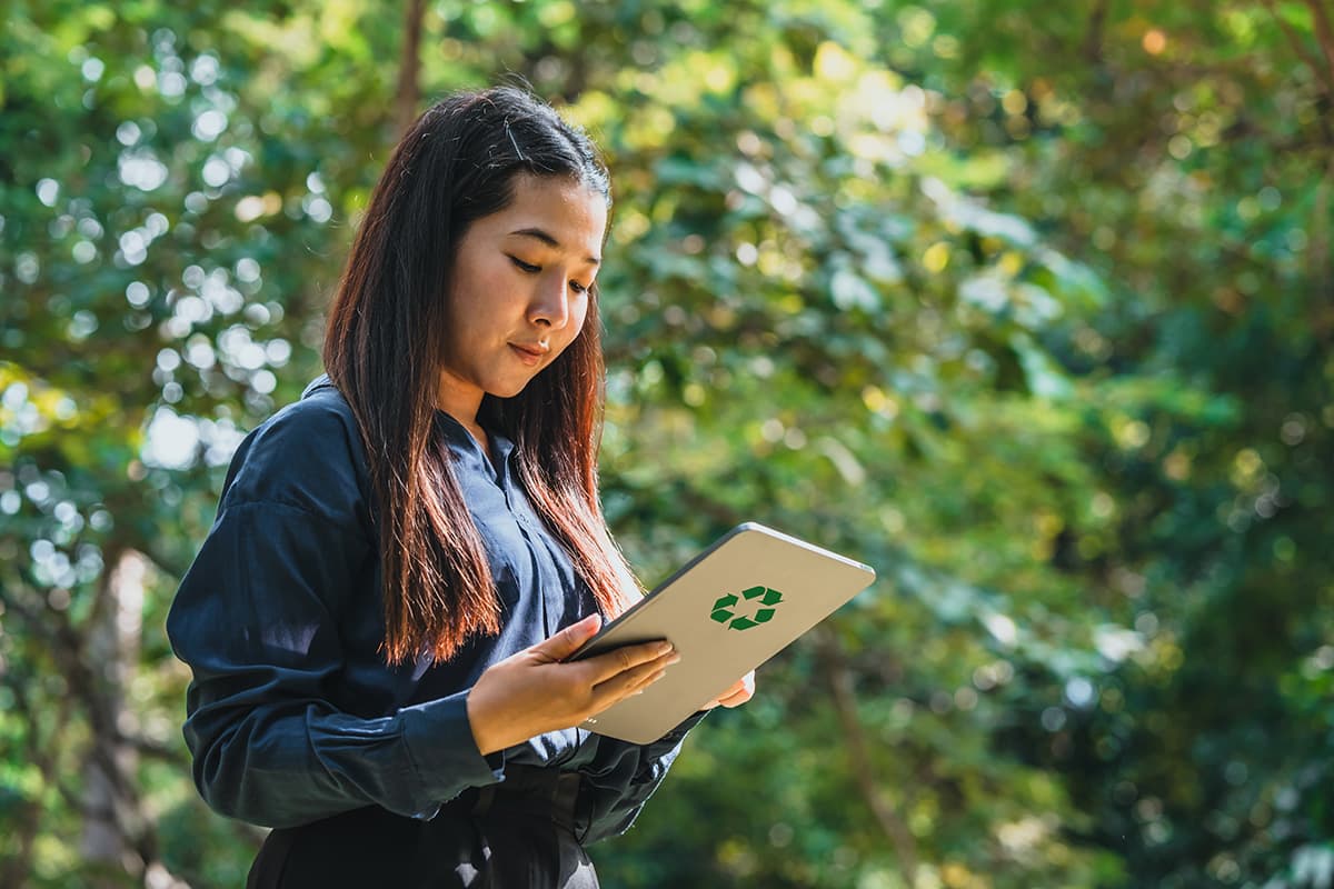 Person standing outdoors and holding a tablet displaying a green recycling symbol