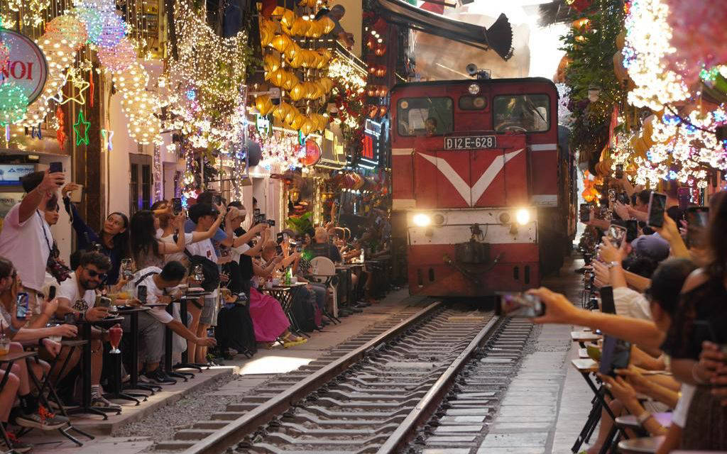 Youngsters and tourists enjoying coffee while watching the train pass by at Hanoi “Train Street” (Photo by: La Casta Cruise)