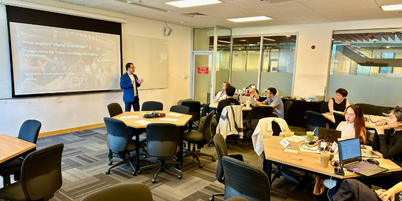Photo of a lecturer teaching in front of a white board titling what makes a digital innovation perspectives on value-creation and digital operations to a group of postgraduate students