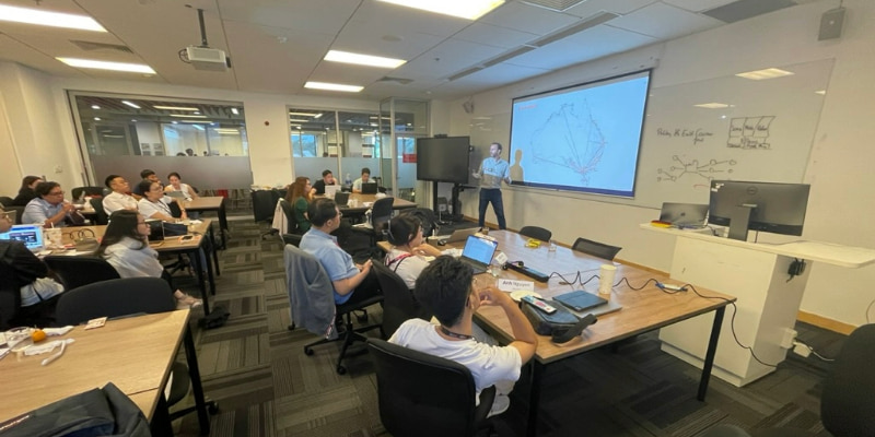 Photo of a lecturer teaching in front of an interactive white board to a group of postgraduate students