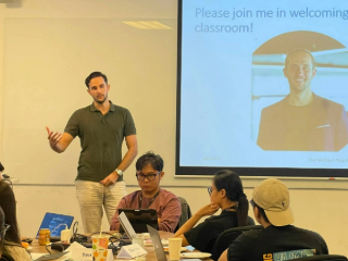 Photo of a guest lecturer presenting in front of the interactive whiteboard to the students who are sitting with their electronic devices