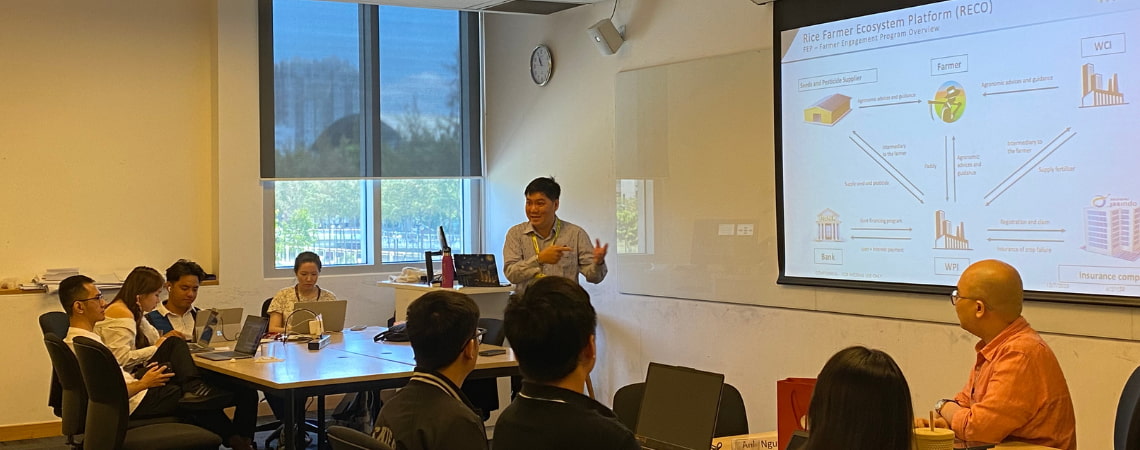 Photo of a guest lecturer presenting in front of the interactive whiteboard titling rice farmer ecosystem platform reco to the students who are sitting with their electronic devices