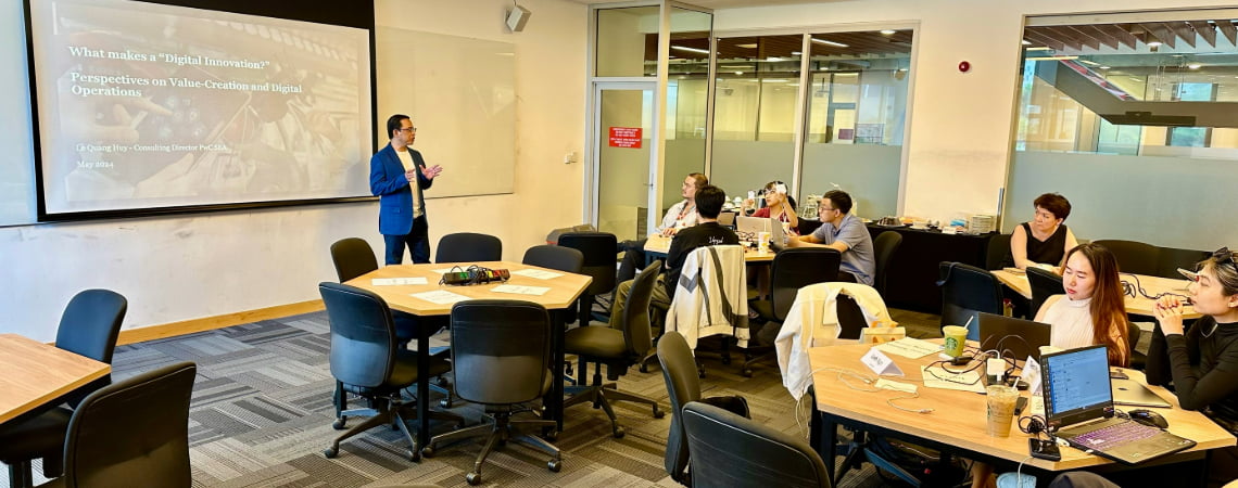 Photo of a lecturer teaching in front of a white board titling what makes a digital innovation perspectives on value-creation and digital operations to a group of postgraduate students
