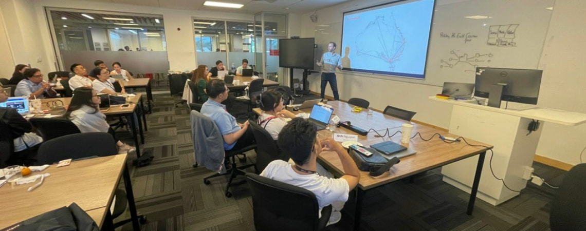 Photo of a lecturer teaching in front of an interactive white board to a group of postgraduate students