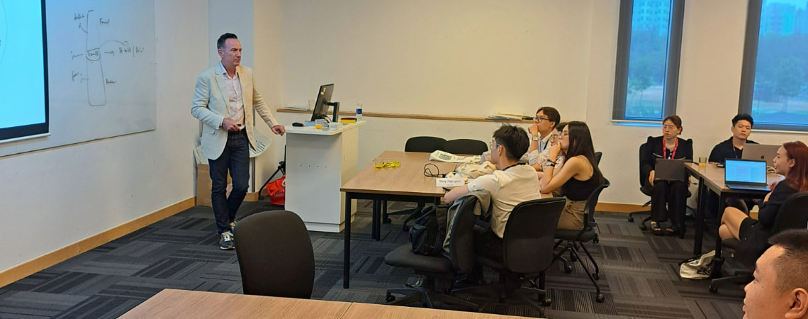 Photo of a lecturer teaching in front of a white board to a group of postgraduate students
