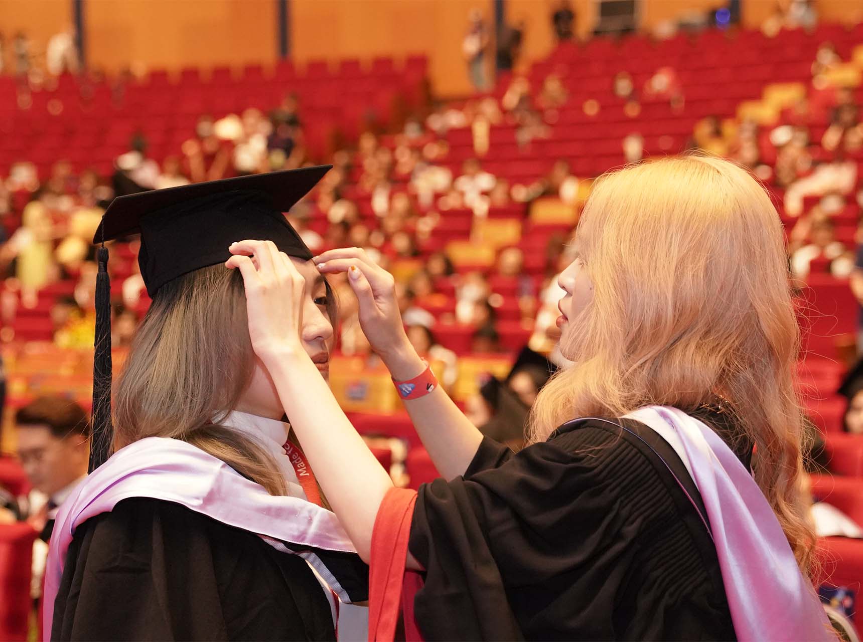 female-student-help-another-student-wear-graduation-gown