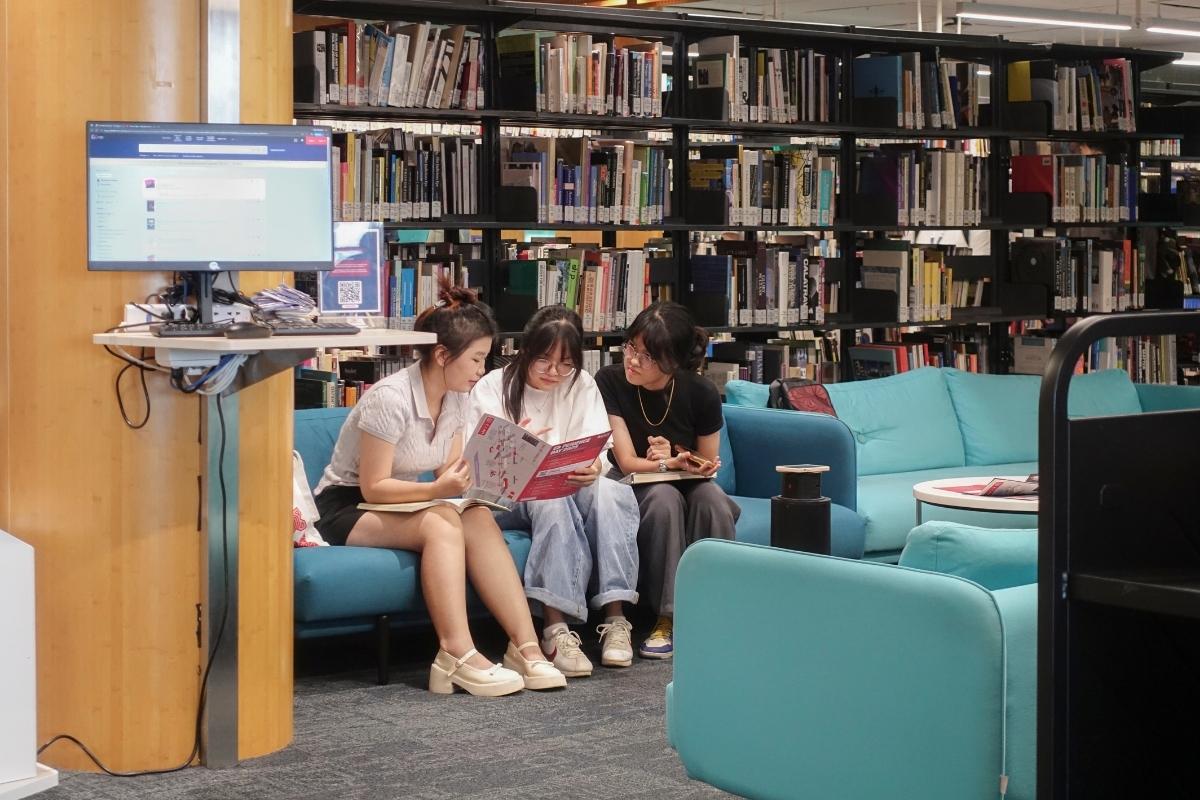The photo showing 3 girls sitting on a coach, together reading a brochure inside a library