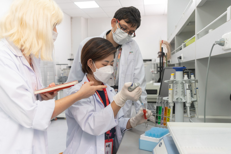 Three lab technicians in white coats and masks working inside a laboratory