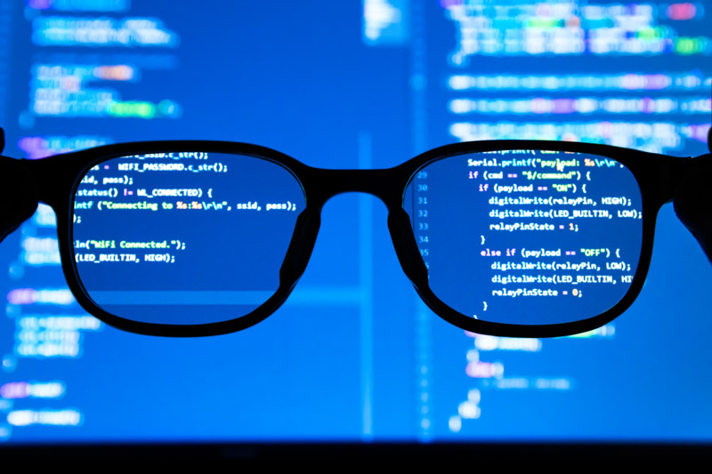 Silhouette glasses in front of laptop computer screen with programming coded.