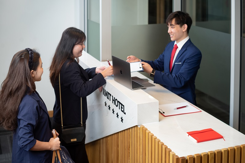 A hotel receptionist receiving two guests at a reception desk.