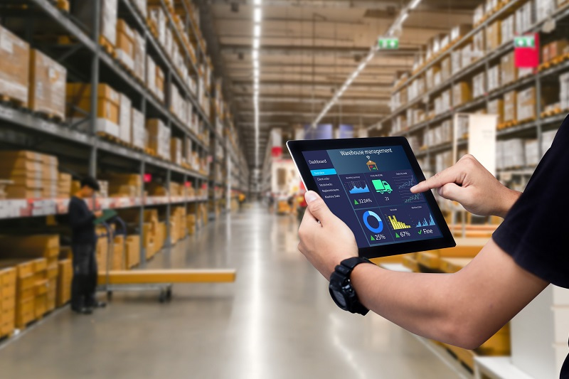 Person touching a tablet with an application saying warehouse management, the person is inside a warehouse