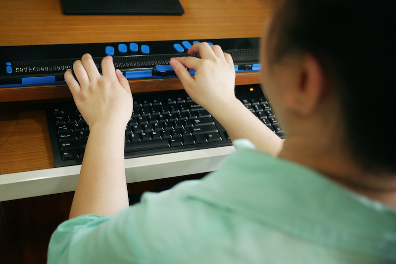 Person with low vision using a Braille display at a computer