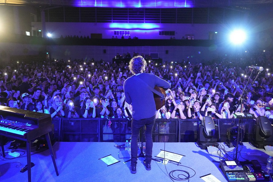 Wide shot of concert audience from behind Dean Lewis on stage