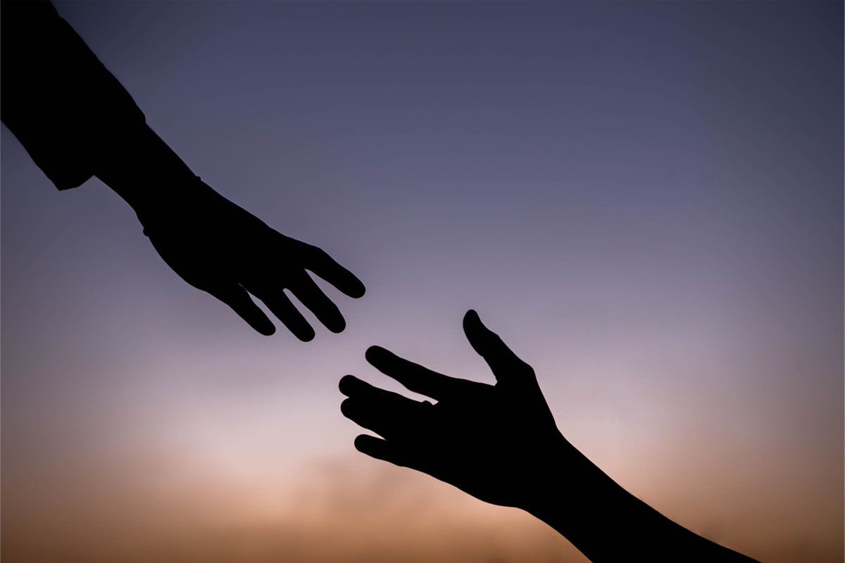 silhouette of two hands teaching out to help each other 